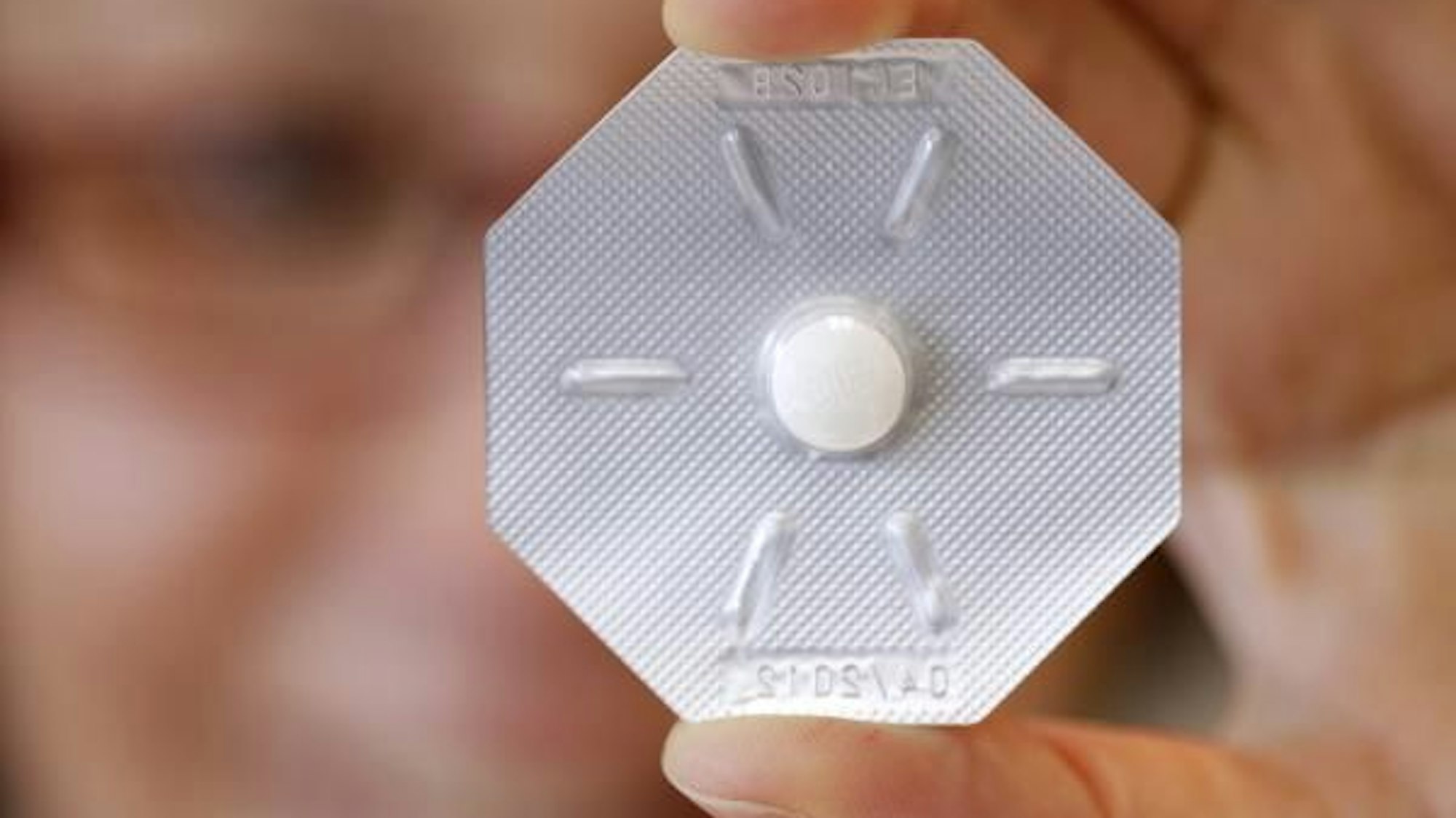 Eine Frau hält ein Tabletten-Blister mit der „Pille danach“ vor ihr Auge.