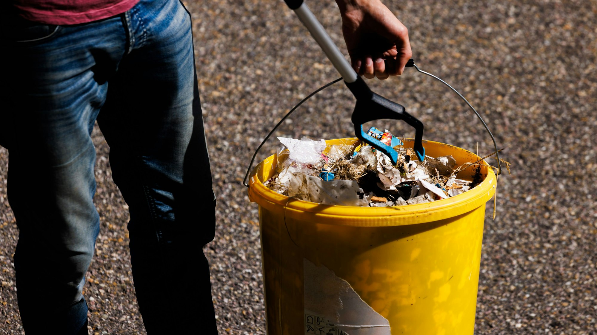 Das Foto zeigt, wie jemand mit einem Müllgreifer Abfall in einen Eimer fallen lässt.