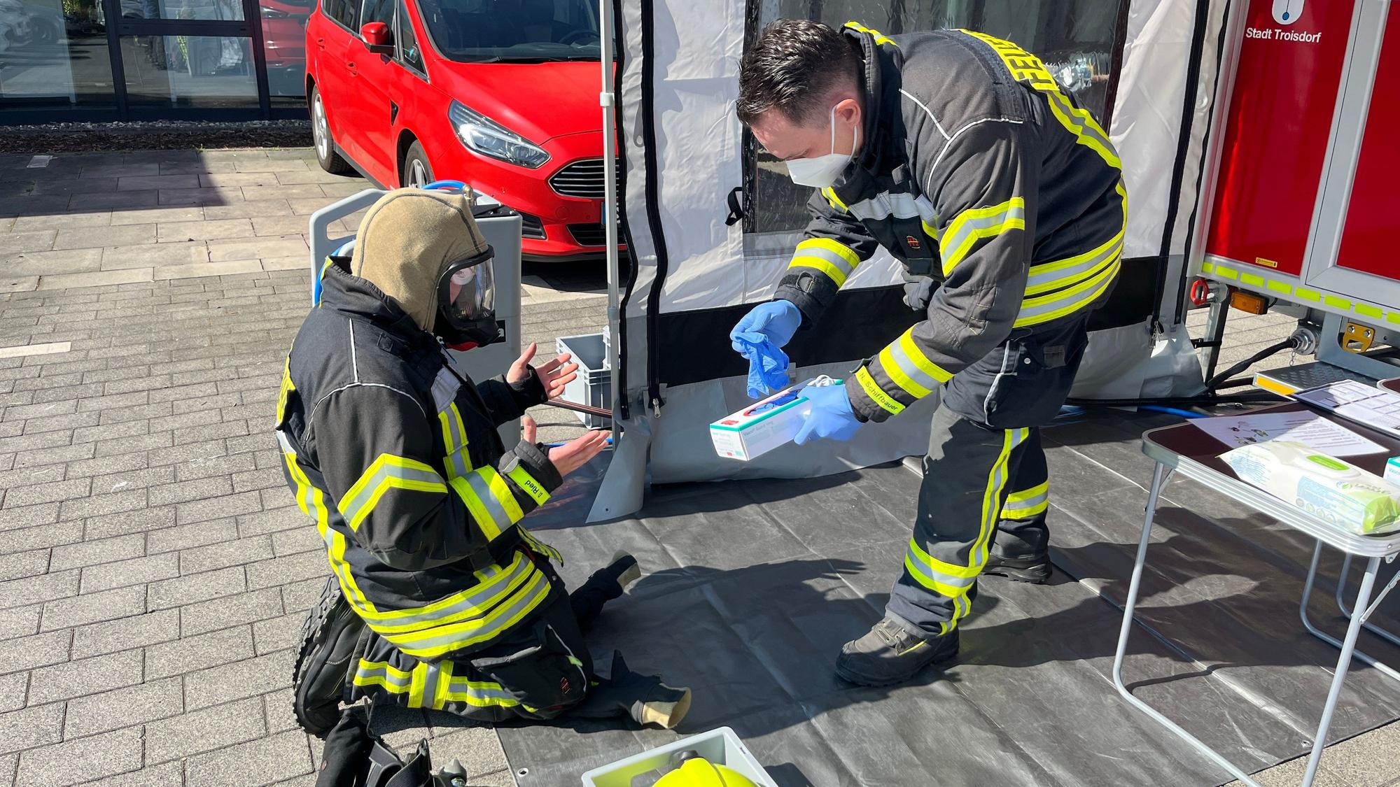 Nico Schiffbauer reicht seinem Kameraden Dennis Ried Einmal-Handschuhe, damit nicht weitere Schadstoffe beim Entkleiden an seine Hände gelangen.