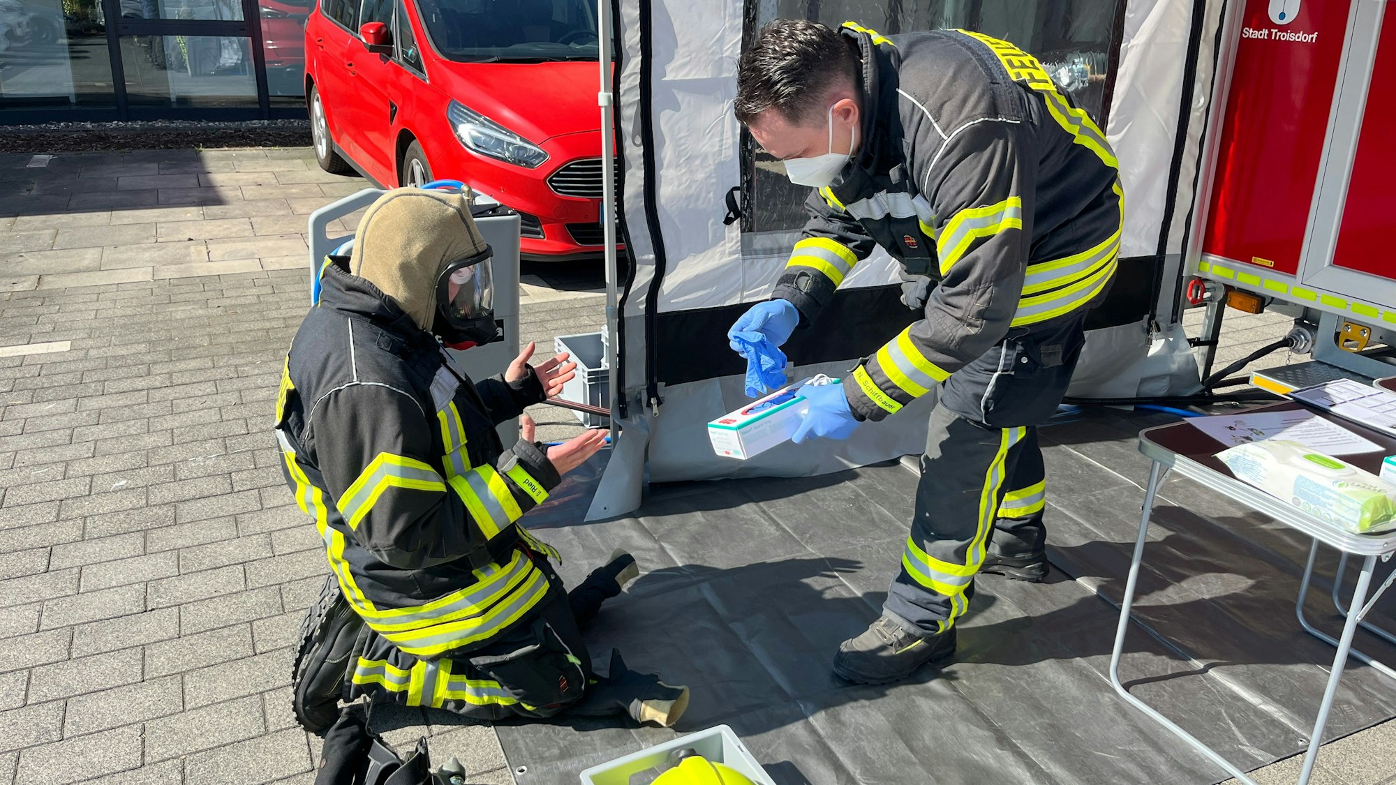 Nico Schiffbauer reicht seinem Kameraden Dennis Ried Einmal-Handschuhe, damit nicht weitere Schadstoffe beim Entkleiden an seine Hände gelangen.