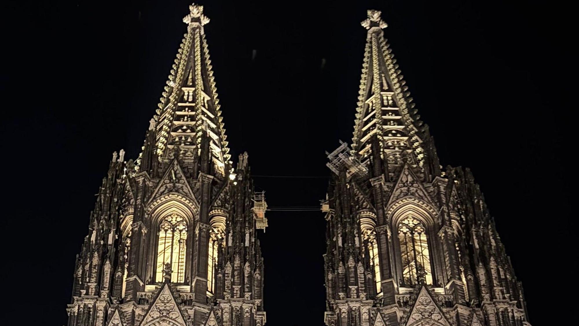 Vor schwarzem Nachthimmel zeigen sich die Spitzen des Kölner Doms, die bis in alle Verzierungen und Erker ausgeleuchtet und klar zu erkennen sind.