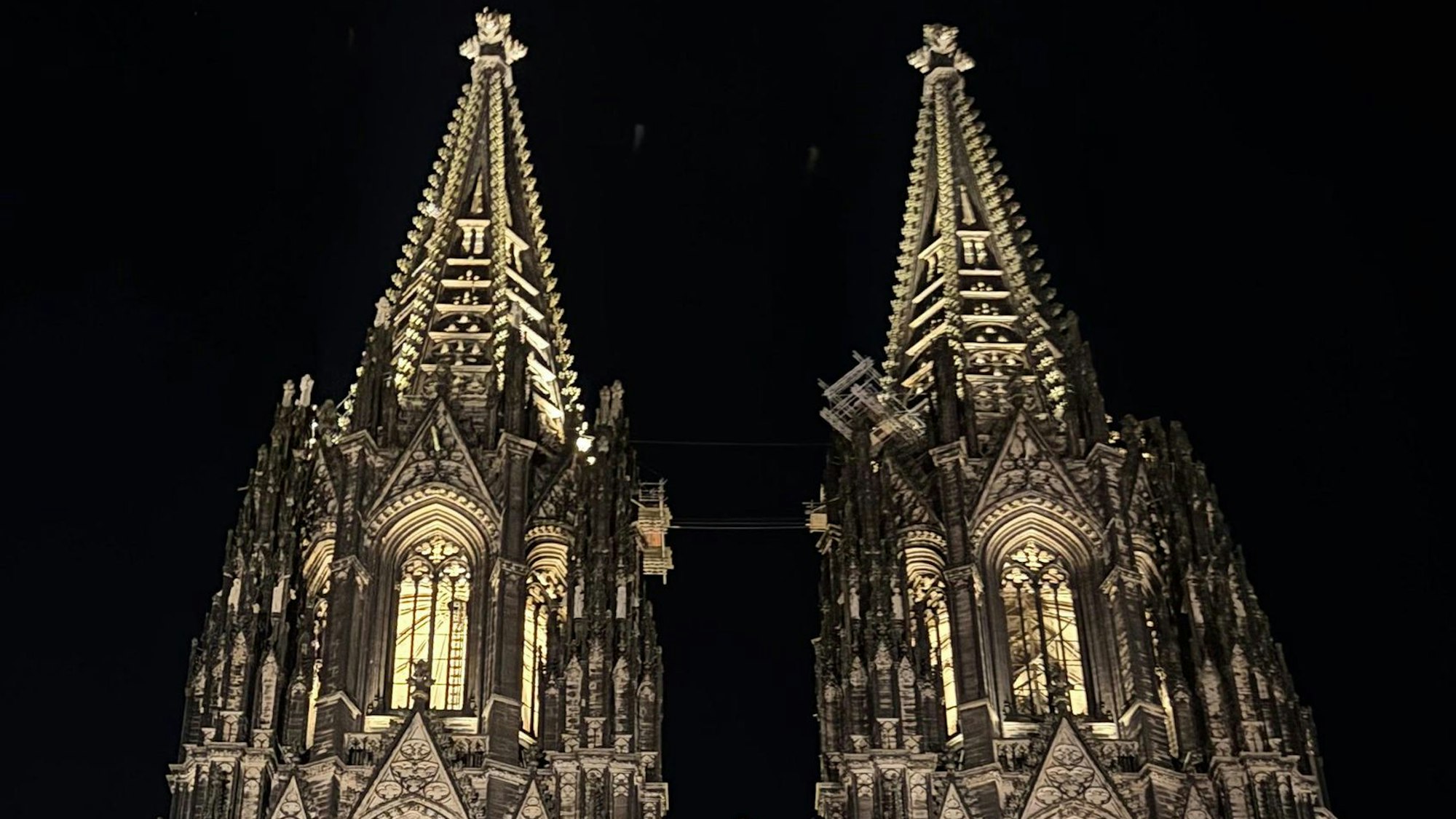 Vor schwarzem Nachthimmel zeigen sich die Spitzen des Kölner Doms, die bis in alle Verzierungen und Erker ausgeleuchtet und klar zu erkennen sind.