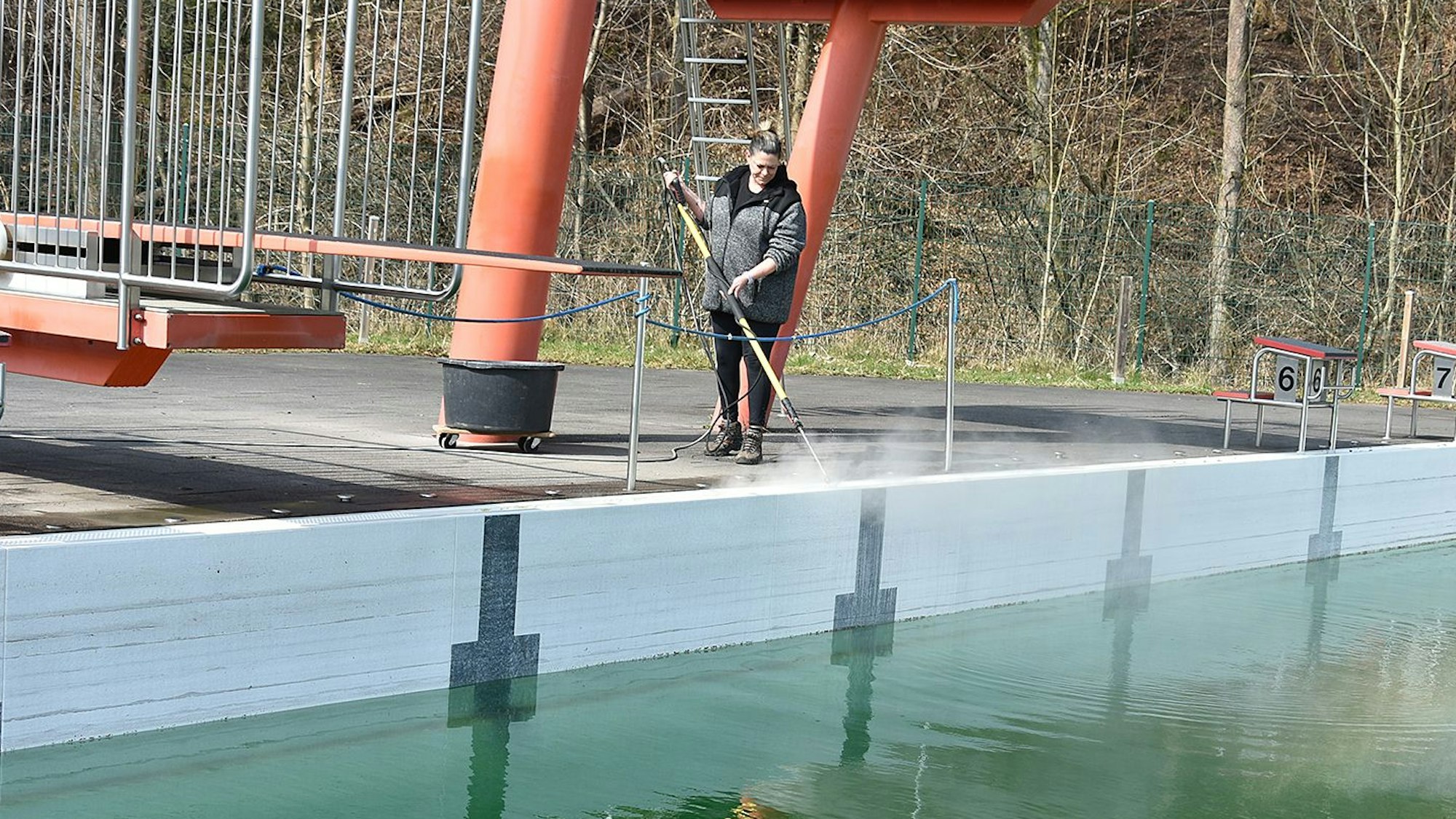 Eine Frau reinigt mit dem Hochdruckreiniger ein Schwimmbecken.