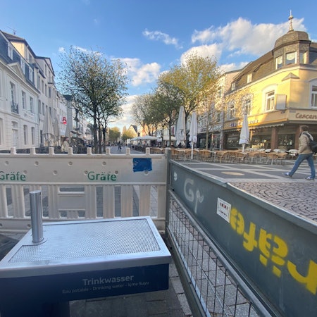 Zu sehen ist einer der Trinkwasserbrunnen, der von einem Bauzaun abgeschirmt wird.