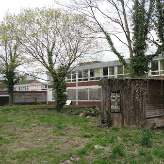 Ein schmuckloser zweistöckiger Bau ist von einer Wiese aus zu sehen.