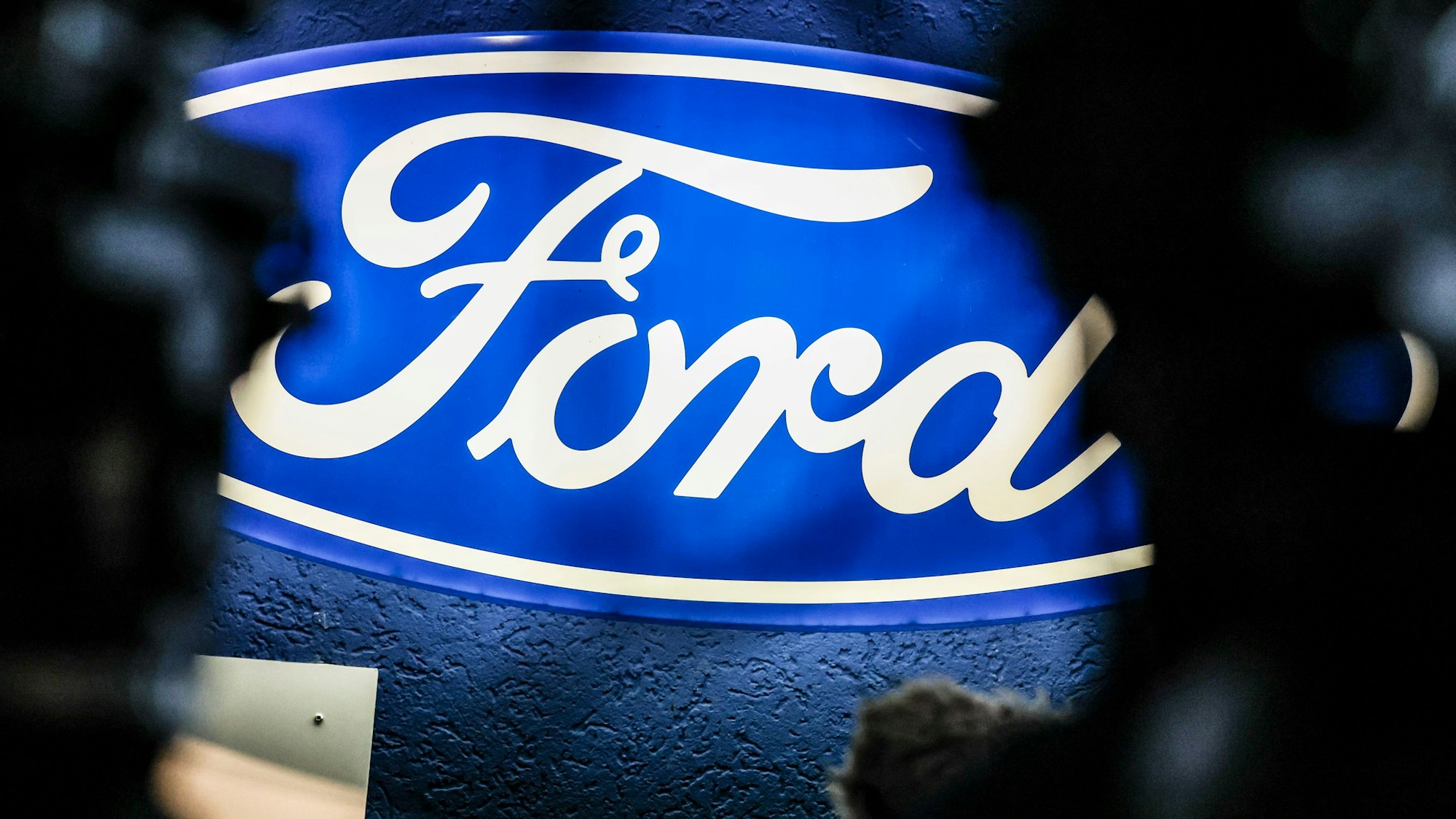 ARCHIV - 10.12.2024, Nordrhein-Westfalen, Köln: Ein beleuchtetes Firmenschild des Autobauers Ford leuchtet am Rande einer Betriebsversammlung am Standort Köln. Nach der Bekanntgabe eines weitreichenden Stellenabbaus beim Autobauer Ford in Köln sprach auch Bundeskanzler Scholz zu den Beschäftigten, von denen viele um ihre Jobs bangen. (zu dpa: «Warnstreiks bei Ford - IG Metall fordert Insolvenzschutz») Foto: Christoph Reichwein/dpa +++ dpa-Bildfunk +++