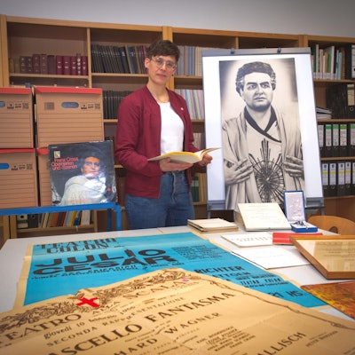 Das Foto zeigt Plakate, Urkunden und Fotos aus dem Nachlass des Opernsängers Franz Crass, dazwischen Stadtarchivarin Sarah Zeppenfeld.