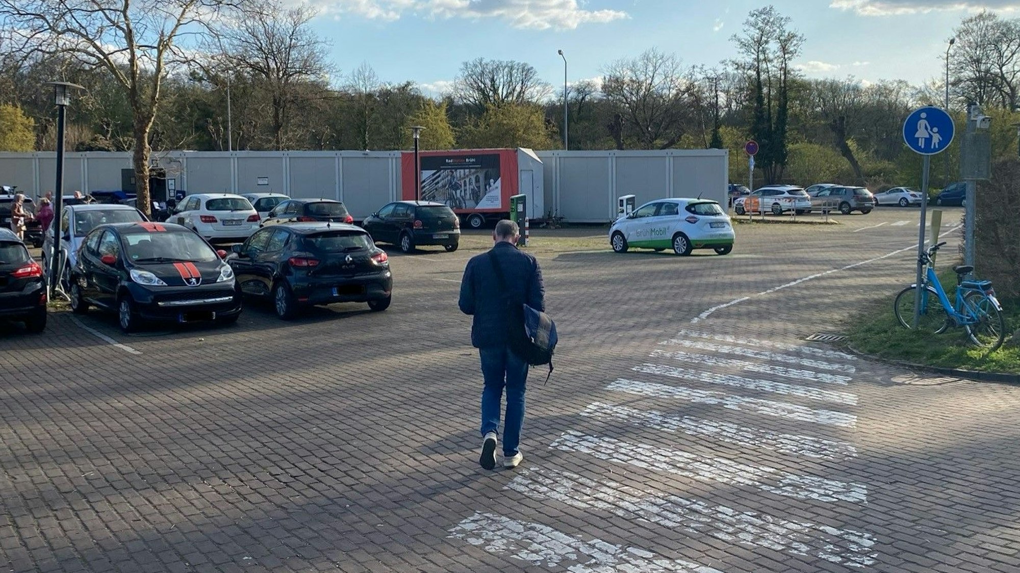 Zu sehen ist ein Mann, der über einen Parkplatz zur provisorischen Radstation geht.