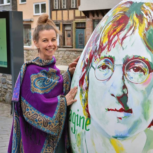 Das Bild zeigt die Künstlerin neben ihrem Werk, auf dem ein Porträt von John Lennon zu sehen ist.