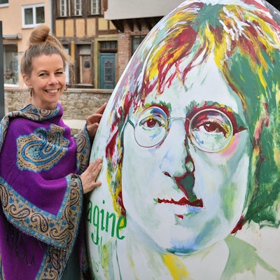 Das Bild zeigt die Künstlerin neben ihrem Werk, auf dem ein Porträt von John Lennon zu sehen ist.