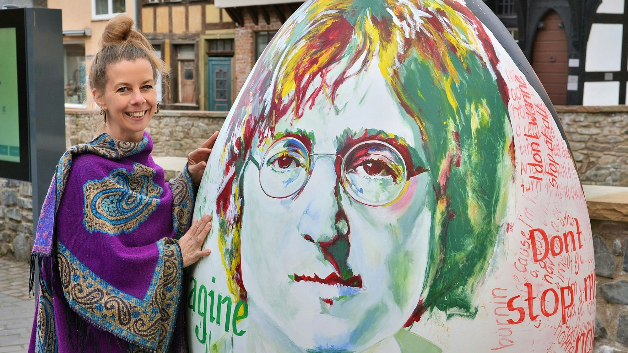 Das Bild zeigt die Künstlerin neben ihrem Werk, auf dem ein Porträt von John Lennon zu sehen ist.