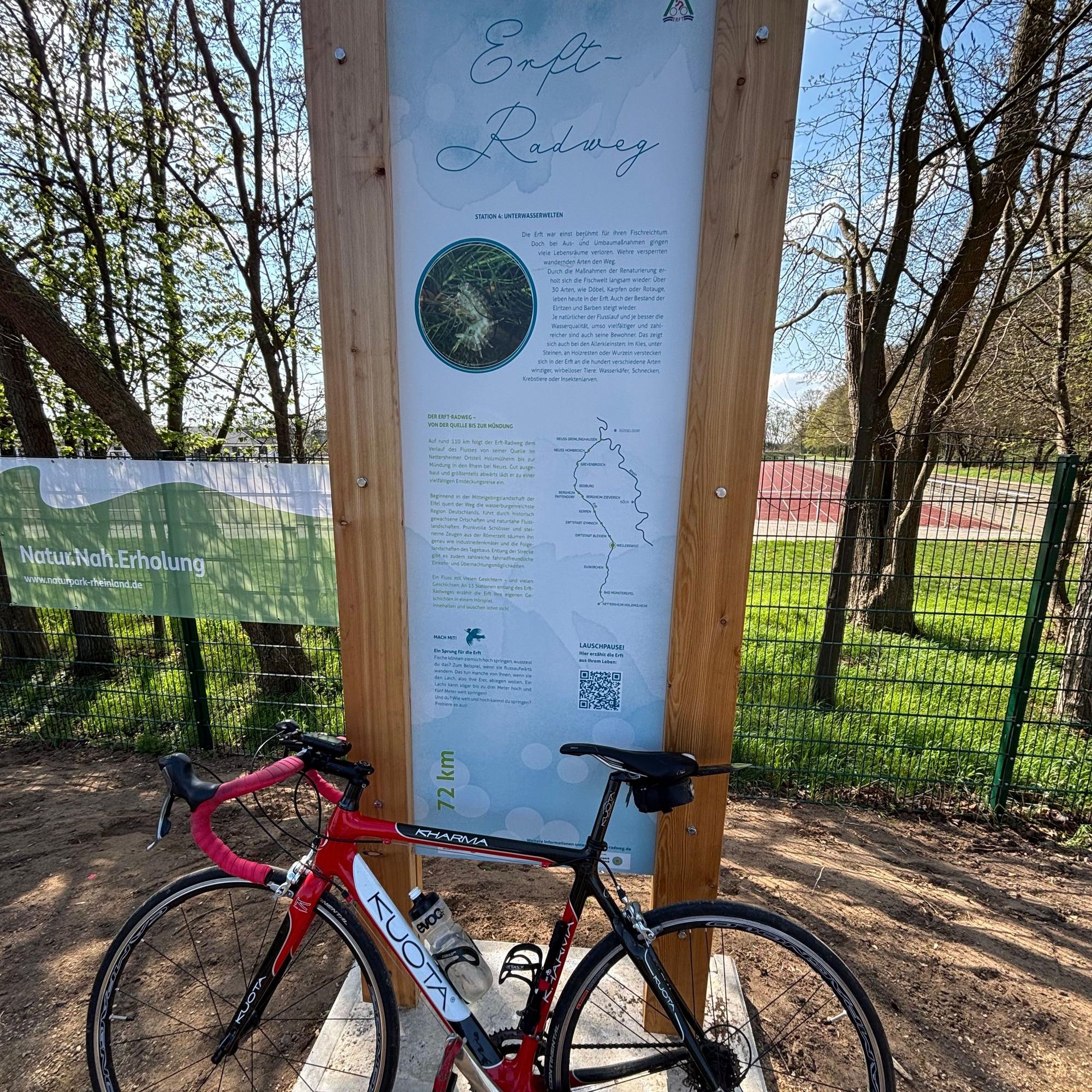Vor einer Infotafel an einem Sportplatz ist ein Fahrrad angelehnt.