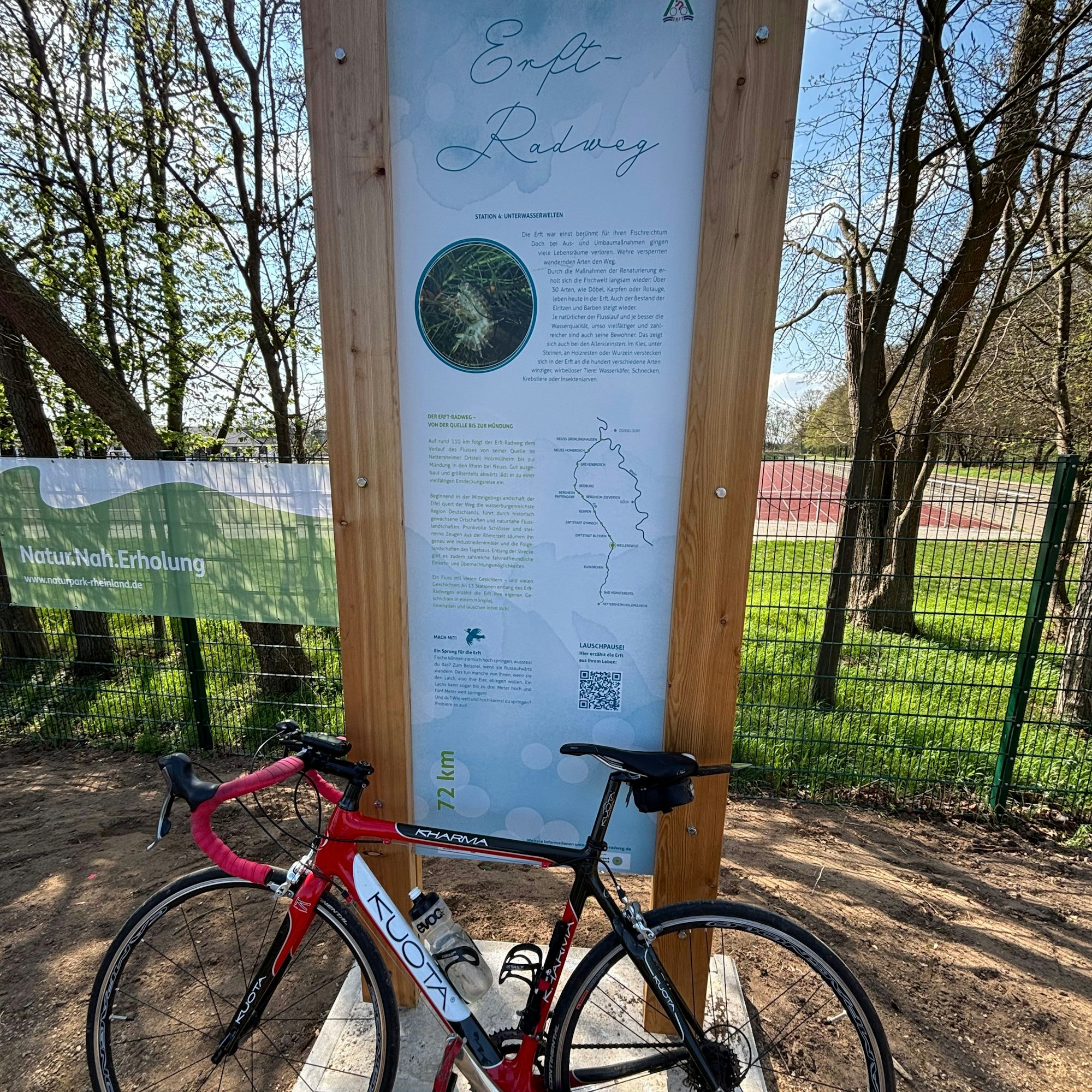 Vor einer Infotafel an einem Sportplatz ist ein Fahrrad angelehnt.