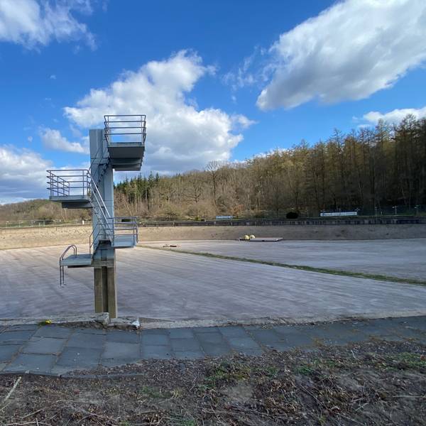 Ein leer gelaufenes, sehr tiefes Schwimmbecken, darin steht ein alter Sprungturm mit drei Ebenen.