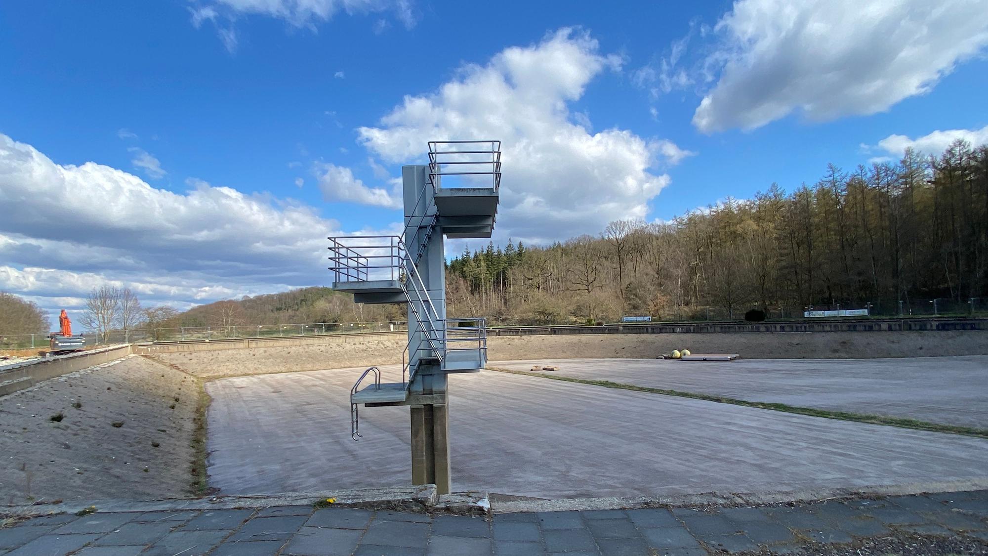 Ein leer gelaufenes, sehr tiefes Schwimmbecken, darin steht ein alter Sprungturm mit drei Ebenen.