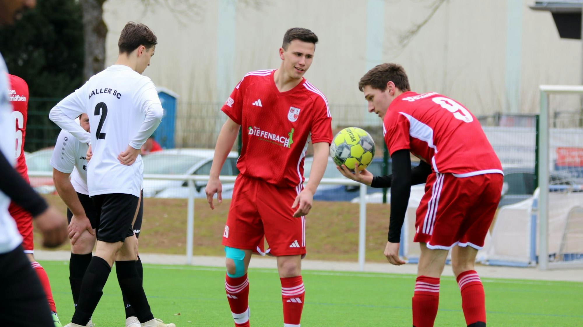 Ein Fußballer von Dahlem-Schmidtheim II hält den Ball in der Hand und legt ihn sich zum Strafstoß hin. Ein Mitspieler spricht mit ihm.