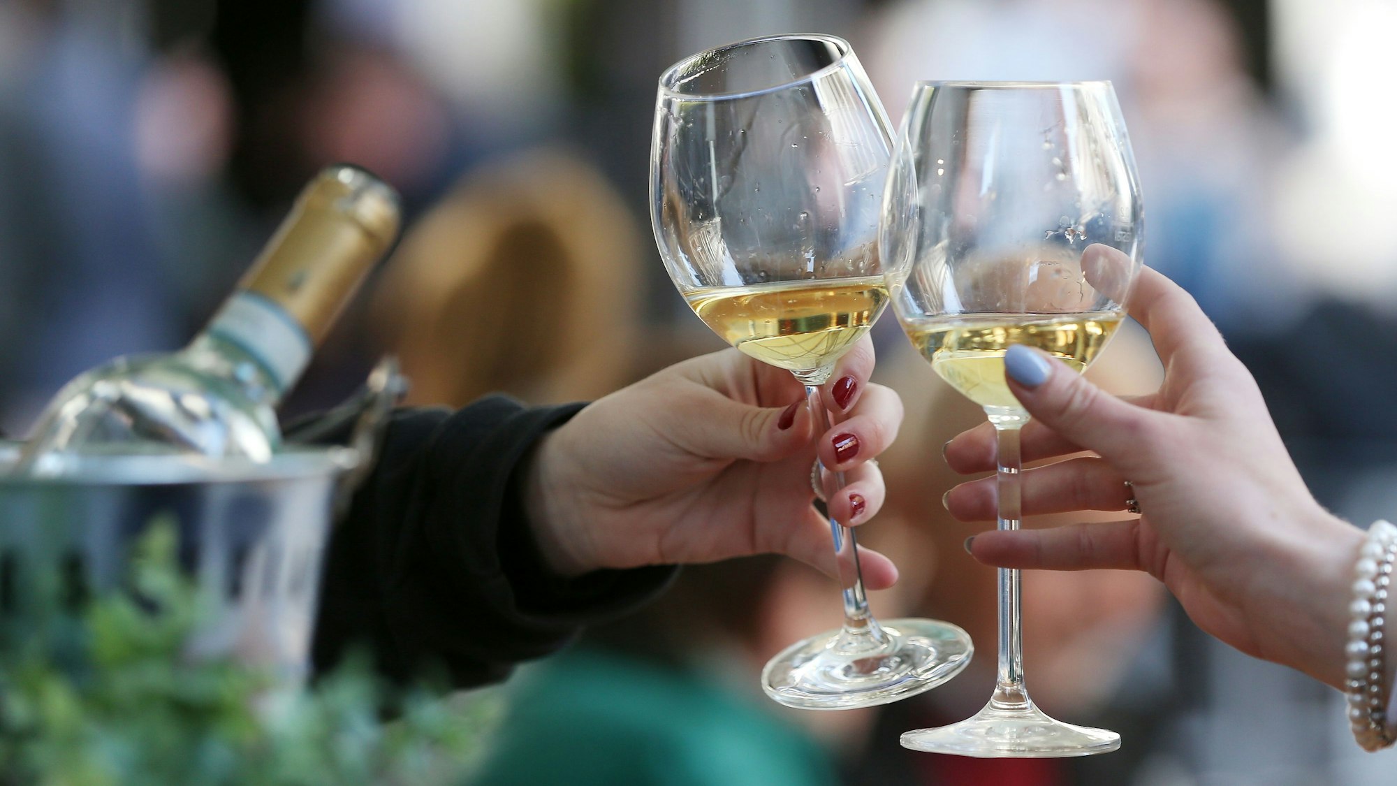 Frauen stoßen an einem Tisch im Außenbereich eines Lokals mit Weißwein an.