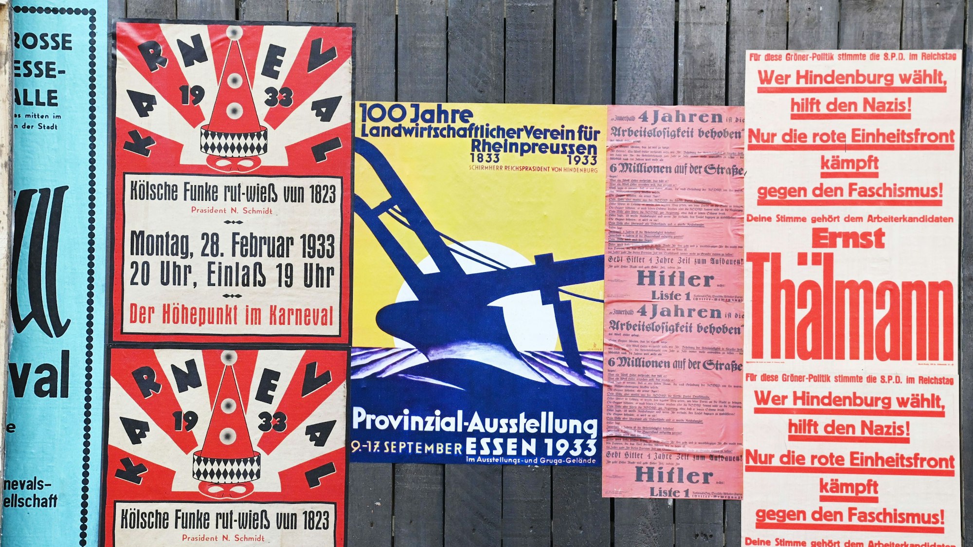 Zu sehen sind fünf bunte, an einem Holzzaun befestigten Plakate, die Inhalte aus den 1930-er Jahren darstellen.