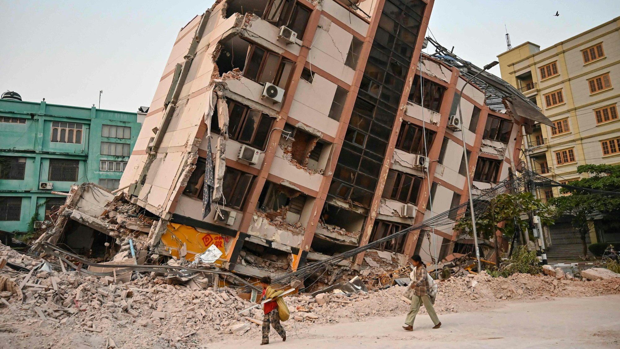 Kinder gehen am 2. April 2025, fünf Tage nach einem schweren Erdbeben in Zentral-Myanmar, an einem eingestürzten Gebäude in Mandalay vorbei. Auch Tage nach einem Erdbeben der Stärke 7,7, bei dem mehr als 2.000 Menschen ums Leben kamen, schlafen viele Menschen in Myanmar noch immer im Freien, da sie entweder nicht in ihre zerstörten Häuser zurückkehren können oder Angst vor weiteren Nachbeben haben. Übersetzt mit DeepL.com (kostenlose Version)