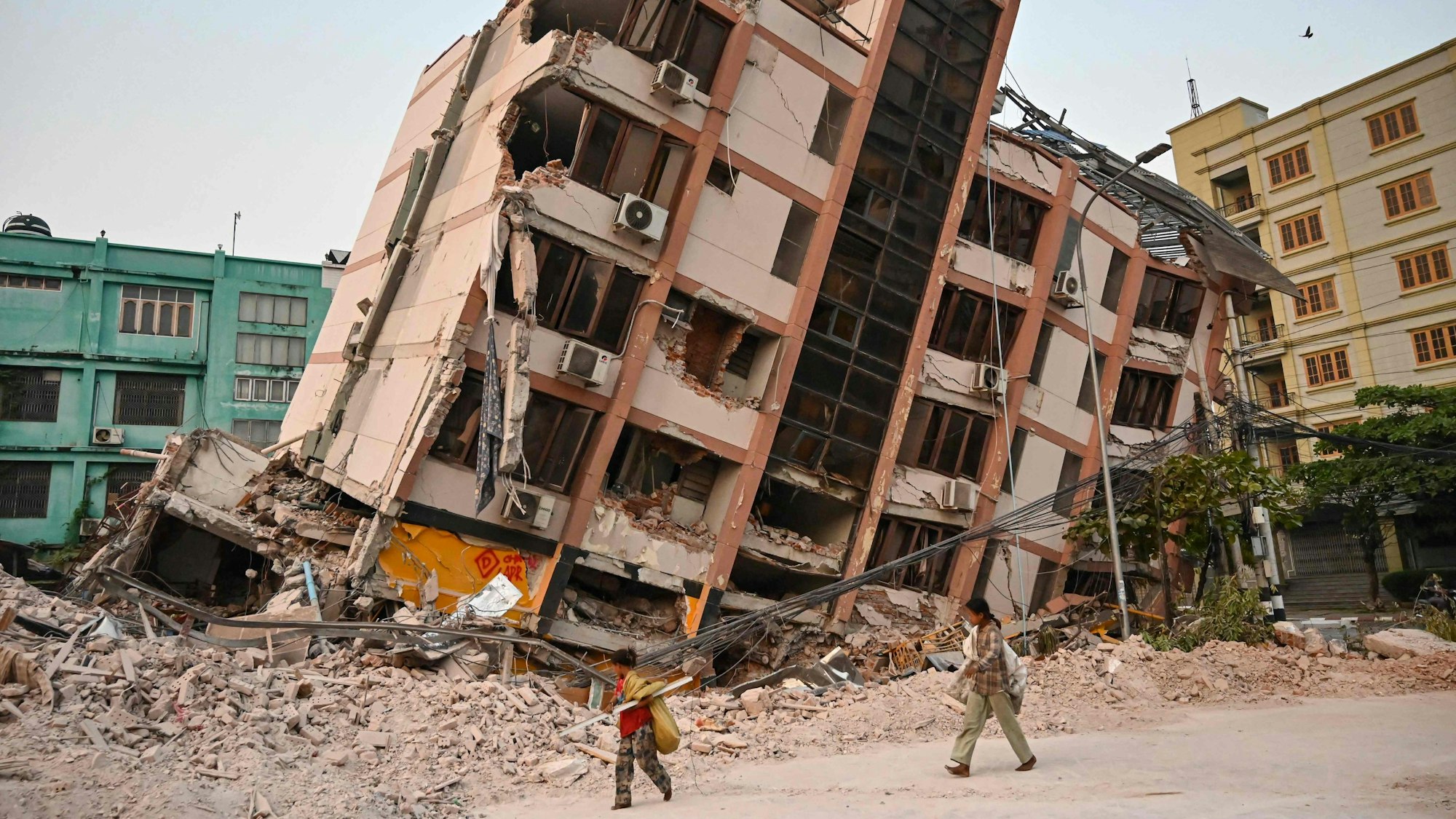 Kinder gehen am 2. April 2025, fünf Tage nach einem schweren Erdbeben in Zentral-Myanmar, an einem eingestürzten Gebäude in Mandalay vorbei. Auch Tage nach einem Erdbeben der Stärke 7,7, bei dem mehr als 2.000 Menschen ums Leben kamen, schlafen viele Menschen in Myanmar noch immer im Freien, da sie entweder nicht in ihre zerstörten Häuser zurückkehren können oder Angst vor weiteren Nachbeben haben. Übersetzt mit DeepL.com (kostenlose Version)