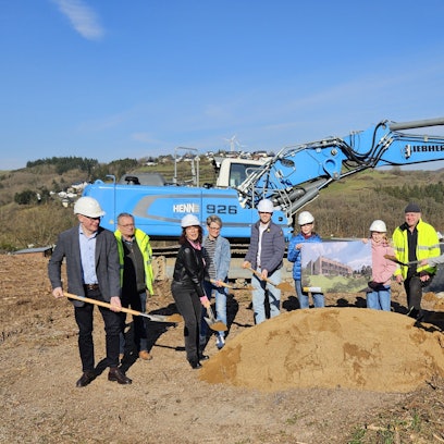 Roswitha Schütt-Gerhards, Thomas Zehnpfennig stehen mit Schülern, Lehrern und Vertretern der Baufirma an einem Sandhaufen und haben Spaten in ihren Händen. Im Hintergrund ist ein Bagger zu sehen.