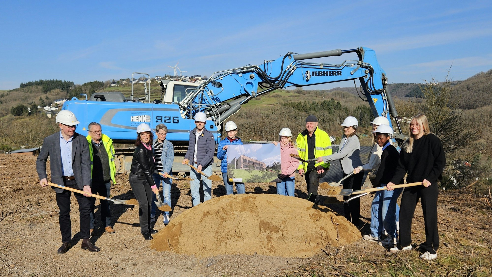 Roswitha Schütt-Gerhards, Thomas Zehnpfennig stehen mit Schülern, Lehrern und Vertretern der Baufirma an einem Sandhaufen und haben Spaten in ihren Händen. Im Hintergrund ist ein Bagger zu sehen.