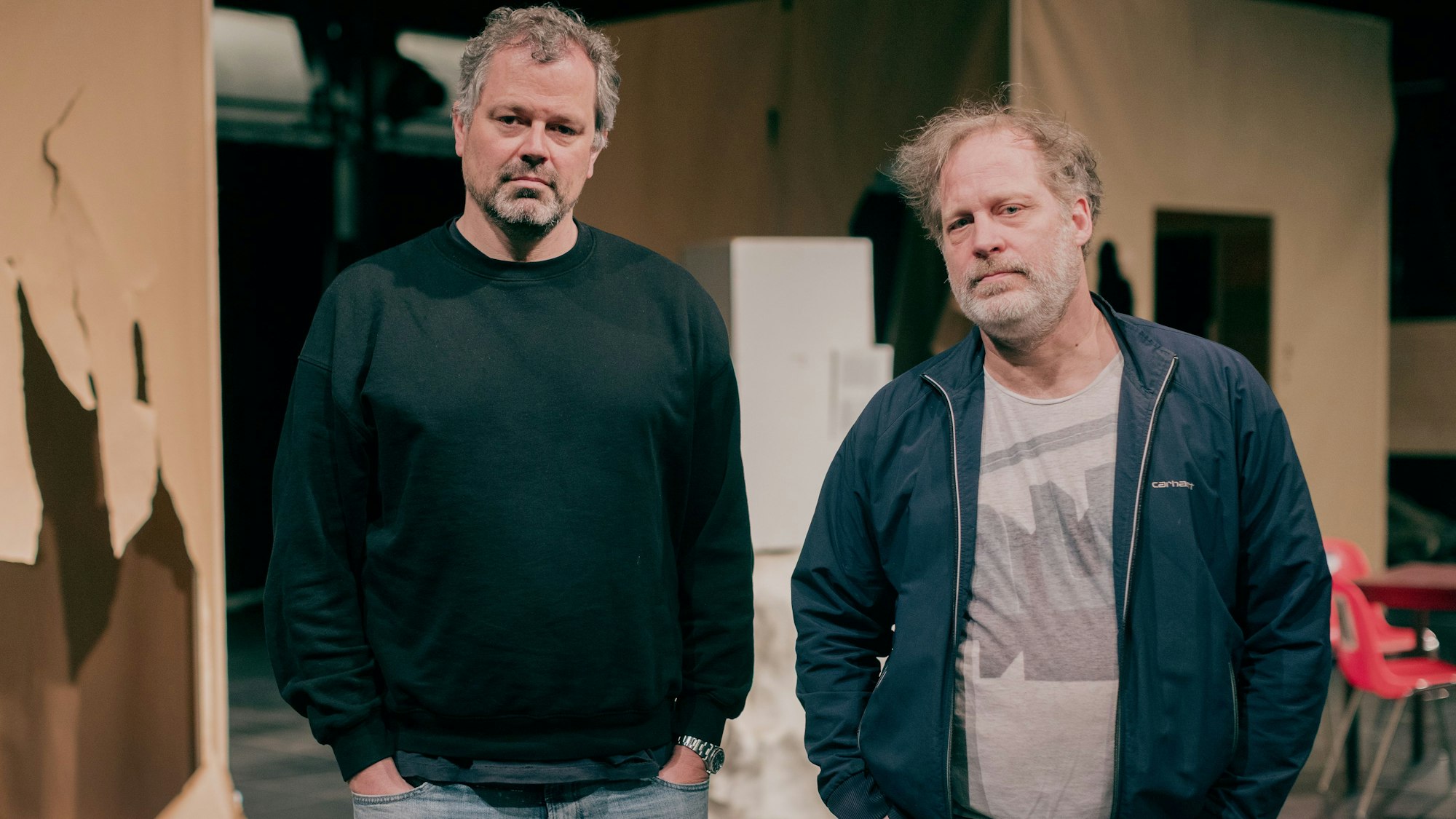 Regisseur Jan Bonny (inks) und Hauptdarsteller Ben Höppner stehen in der Halle Kalk vor den Kulissen der Inszenierung "Eisenfaust".