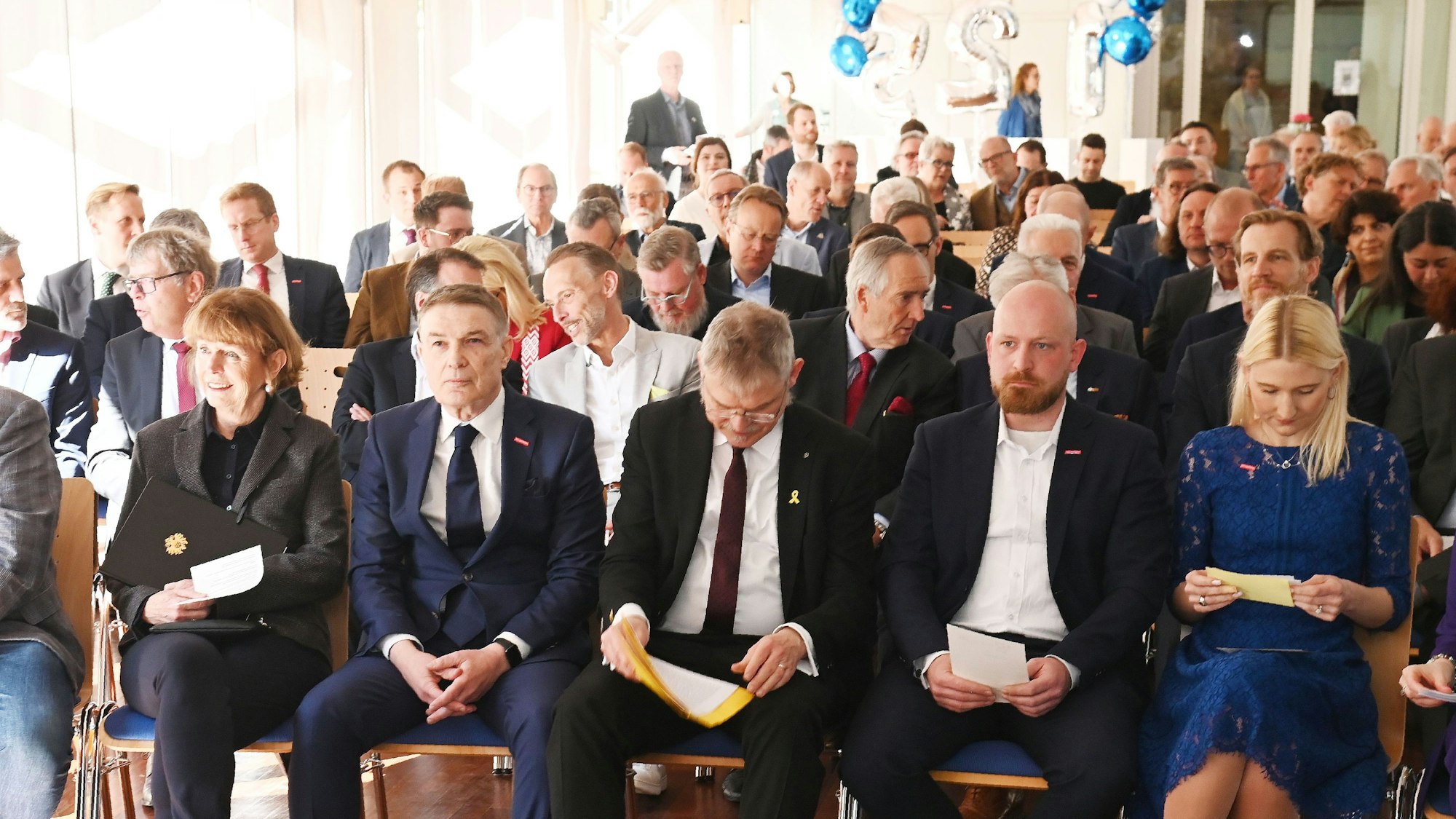 Rund 120 geladene Gäste sitzen in einem Saal.