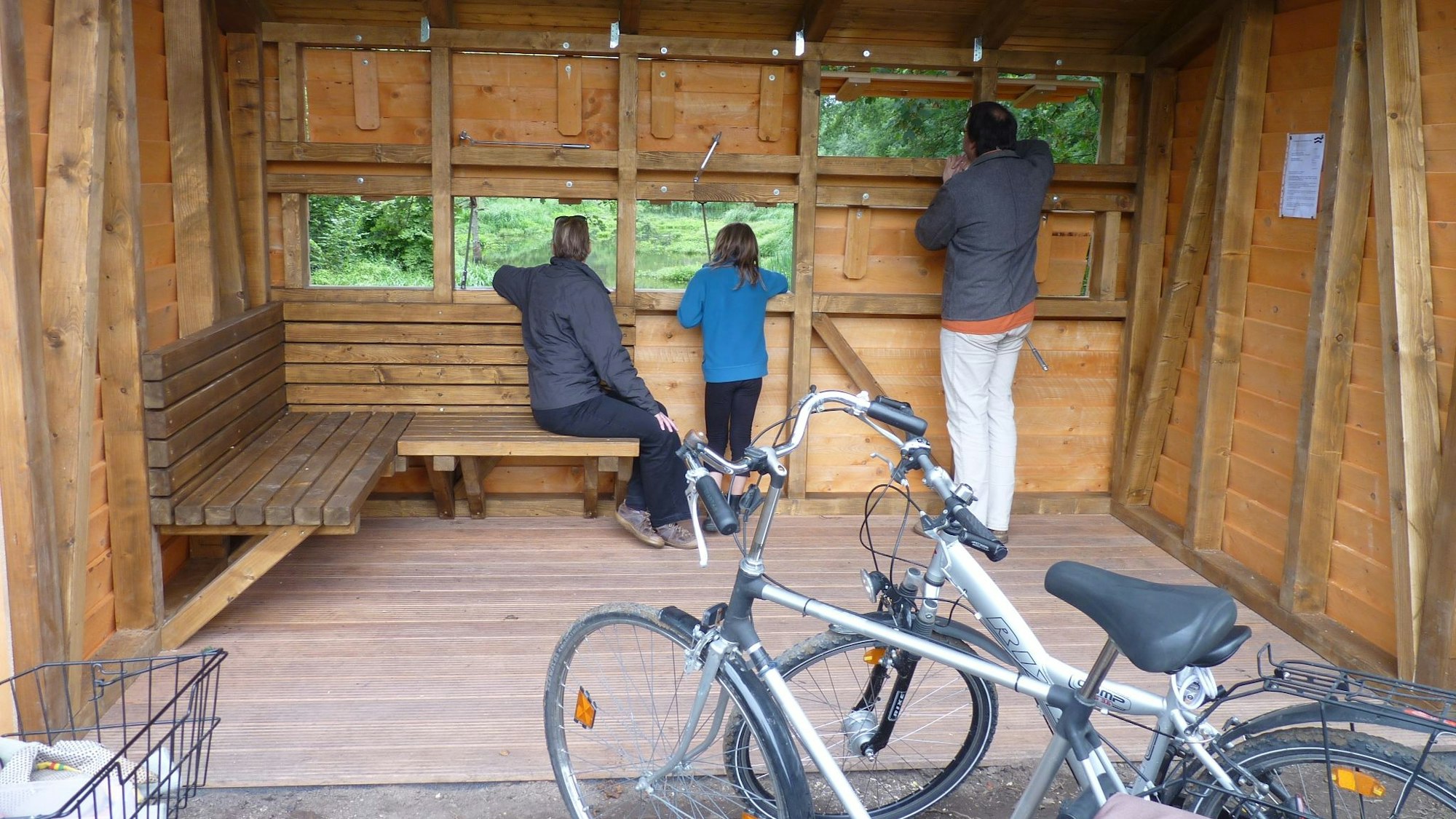 Ein Holzhäuschen mit Fenstern, die den Blick auf ein Biotop ermöglichen.
