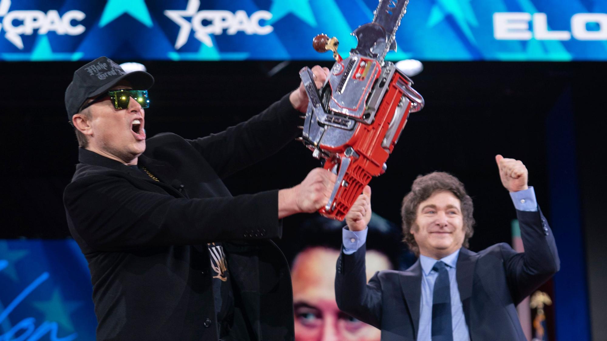 Elon Musk hält eine Kettensäge hoch, die er vom argentinischen Präsidenten Javier Milei (r) erhalten hat.