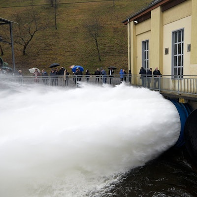 Zahlreiche Personen beobachten, wie eine gewaltige Wasserfontäne aus dem Grundablass der Rurtalsperre schießt.