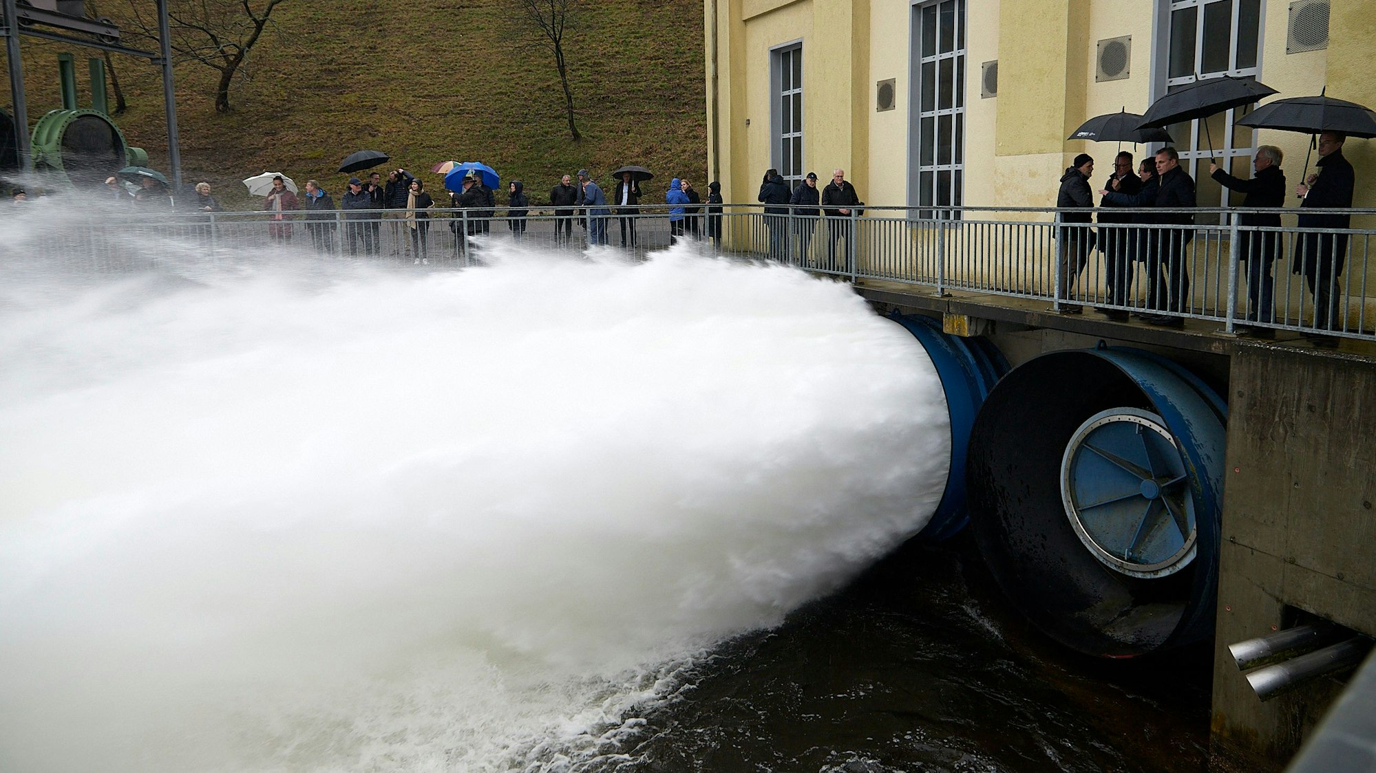 Zahlreiche Personen beobachten, wie eine gewaltige Wasserfontäne aus dem Grundablass der Rurtalsperre schießt.