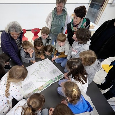 Zahlreiche Kinder und eine Frau schauen auf einen Plan für den neuen Schulhof in Nettersheim-Marmagen.