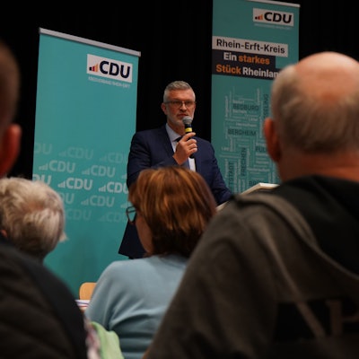 Auf dem Foto ist Harald Stingl im Anzug zu sehen, der in ein Mikrofon spricht.