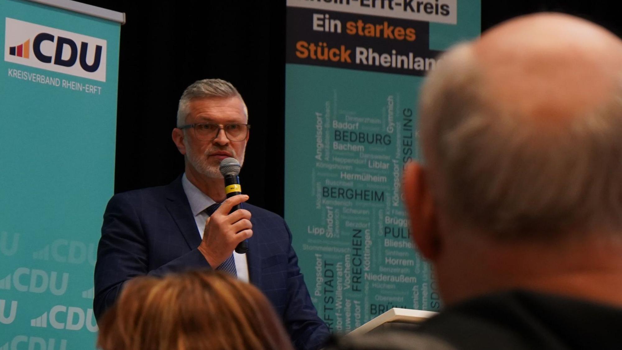 Auf dem Foto ist Harald Stingl im Anzug zu sehen, der in ein Mikrofon spricht.
