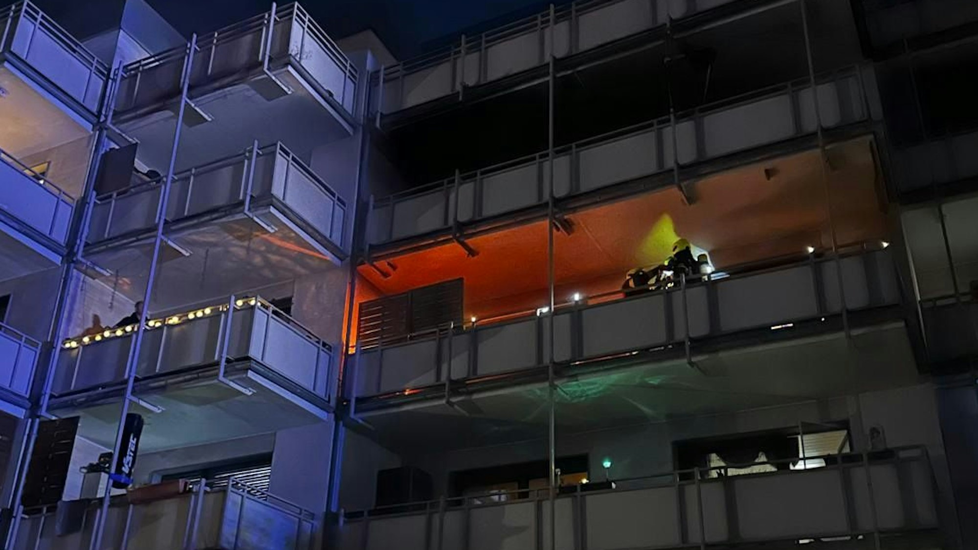 Auf dem Bild ist ein Teil eines brennenden Balkons zu sehen, der von Feuerwehrleuten gelöscht wird.