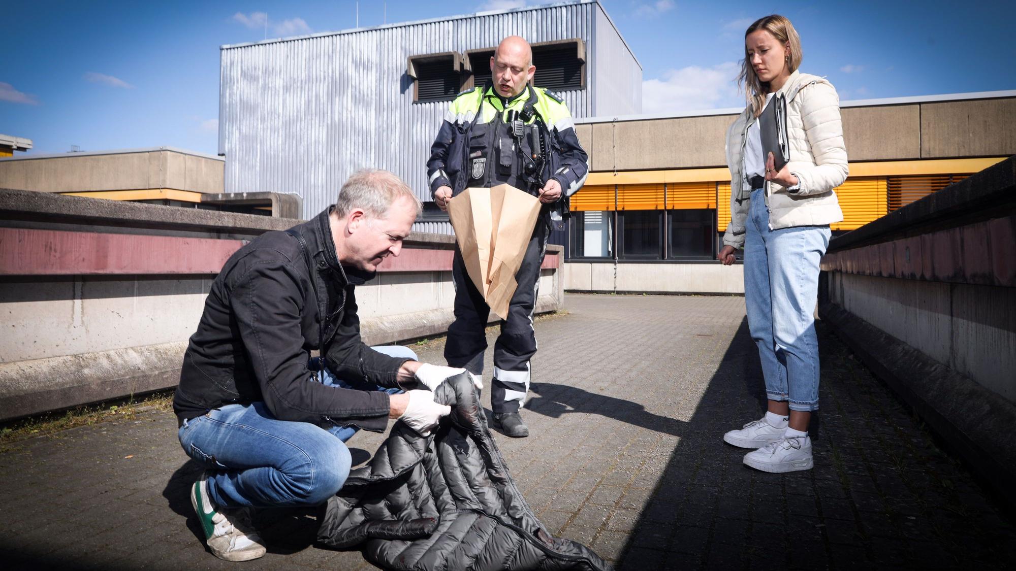 Christian Berg (mitte), Kommissarin Imke und Kommissar Volker sind auf dem Campus der TH. Kommissar Volker trägt Handschuhe und hält eine Daunenjacke prüfend hoch.