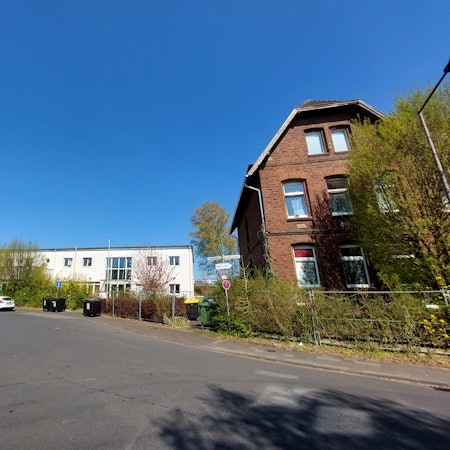 Ein altes Backsteingebäude am rechten Bildrand. Im Hintergrund stehen flache weiße Gebäude .