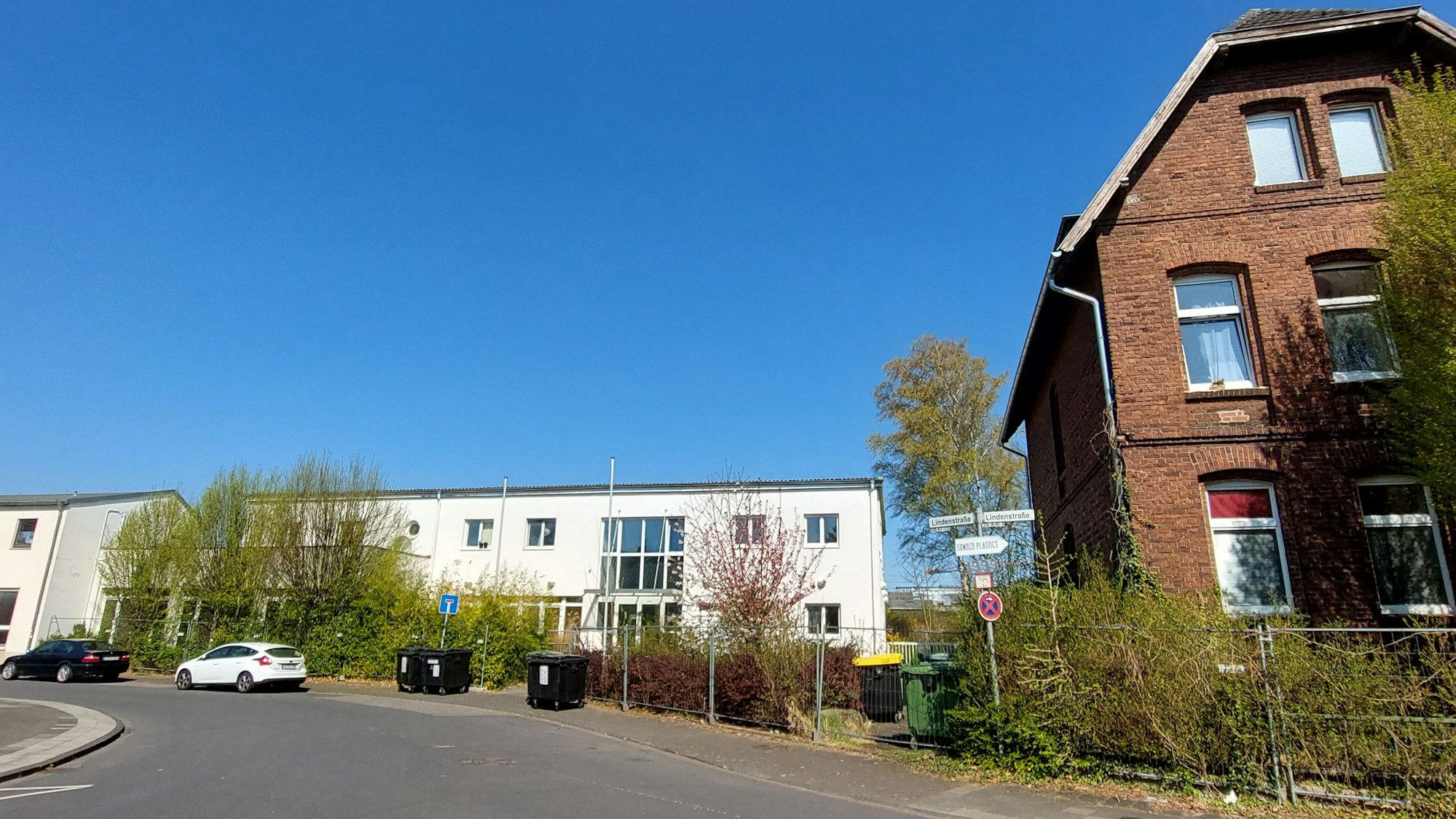 Ein altes Backsteingebäude am rechten Bildrand. Im Hintergrund stehen flache weiße Gebäude .