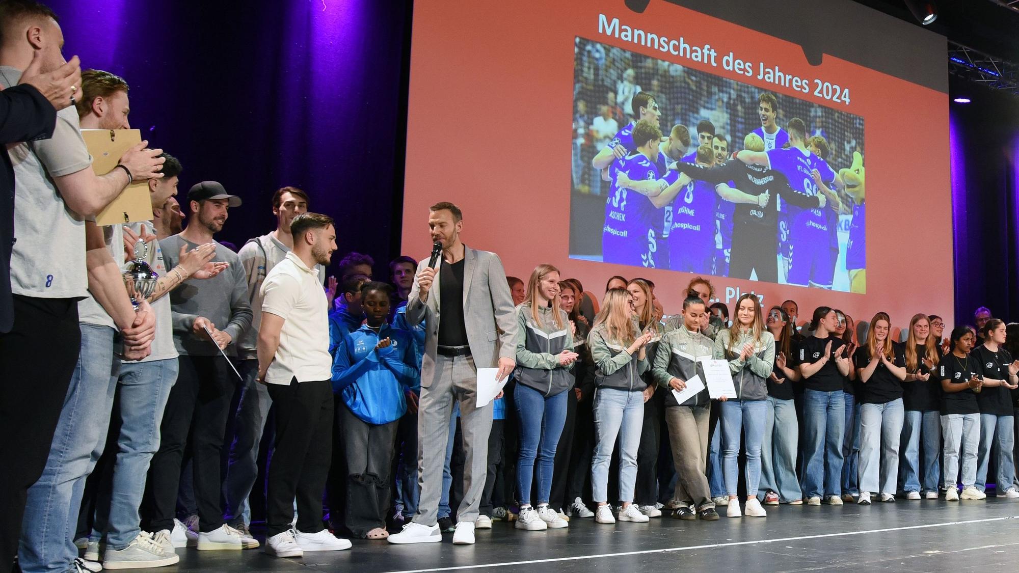 Blick auf einen Moderator, der auf einer Bühne Menschen interviewt.
