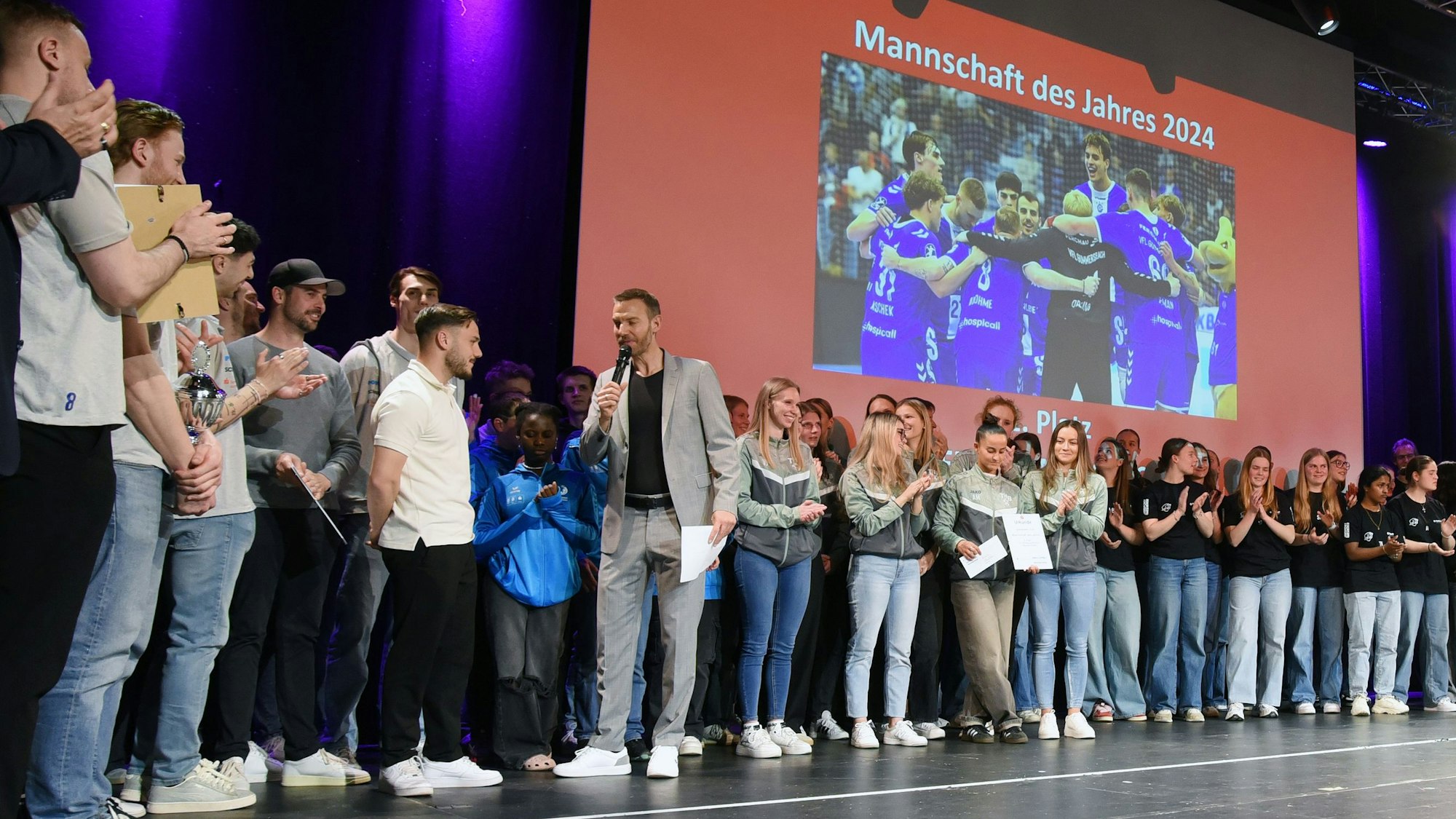 Blick auf einen Moderator, der auf einer Bühne Menschen interviewt.