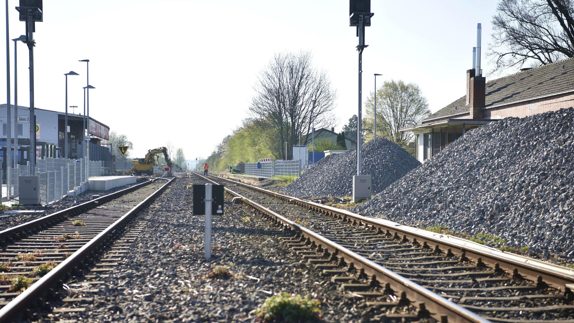 Gleisschotter liegt in großen Haufen neben den Schienen am Bahnhof Zülpich. Im Hintergrund arbeiten ein paar Bauarbeiter auf den Gleisen.