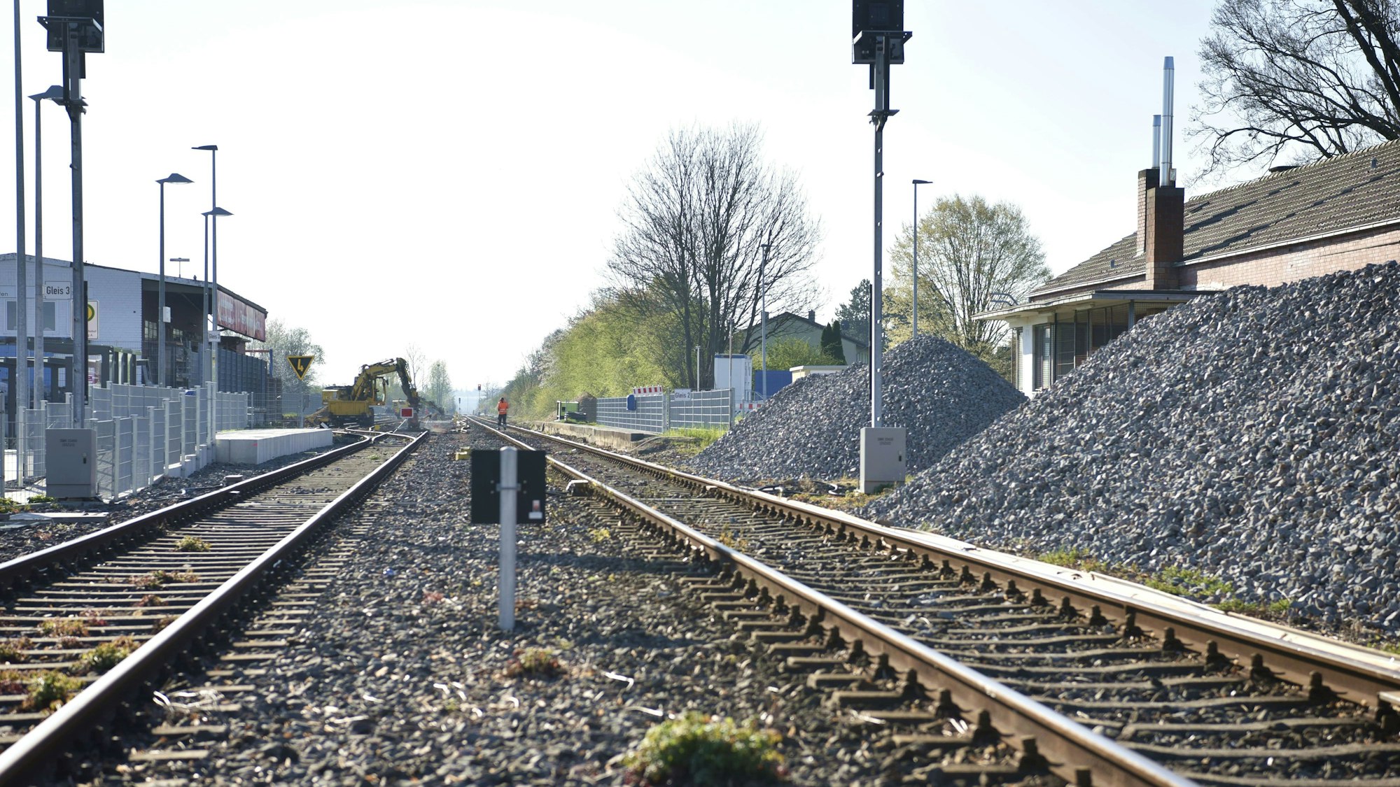 Gleisschotter liegt in großen Haufen neben den Schienen am Bahnhof Zülpich. Im Hintergrund arbeiten ein paar Bauarbeiter auf den Gleisen.