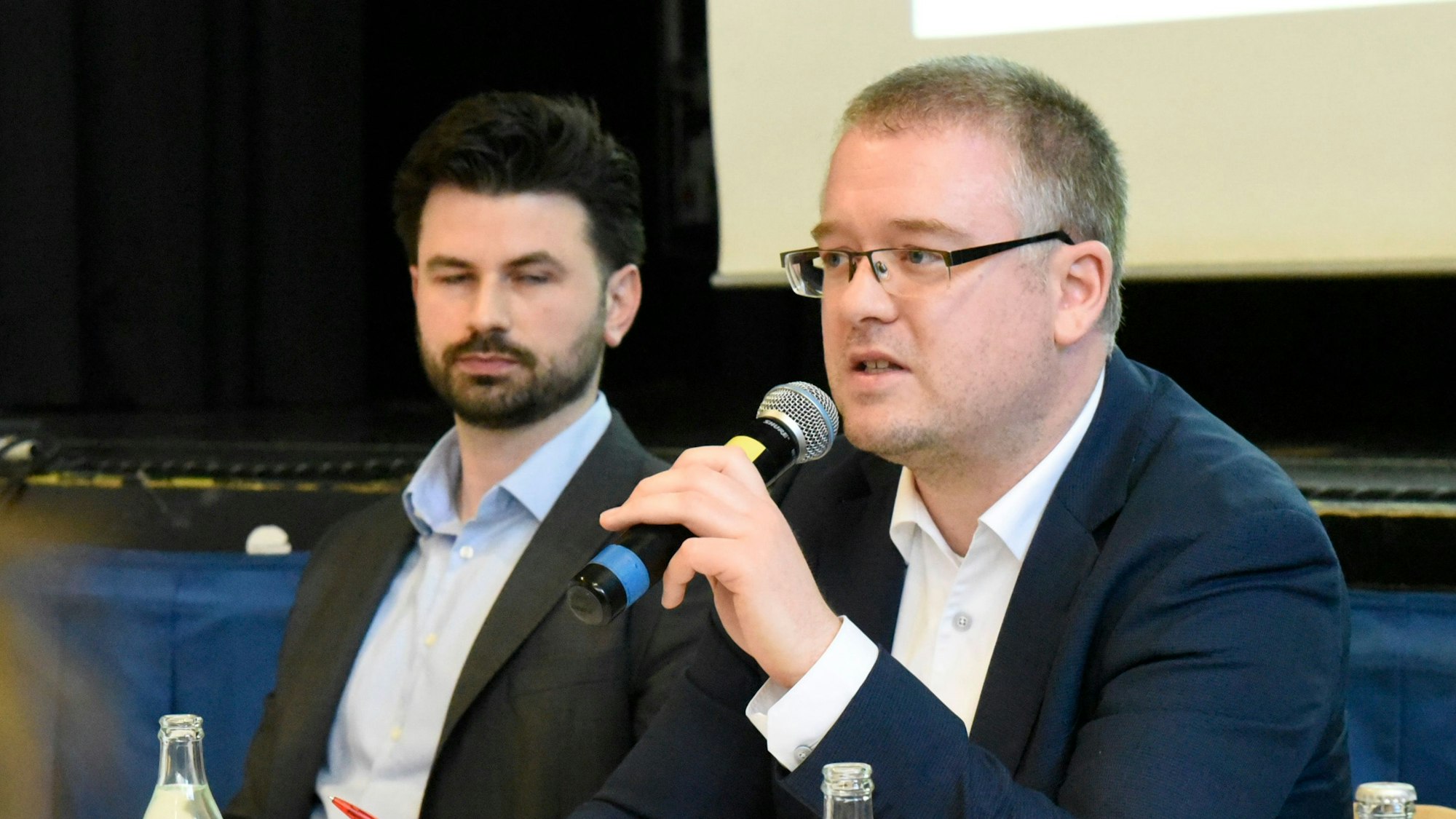 Zu sehen sind zwei Männer, einer spricht in ein Mikrofon.