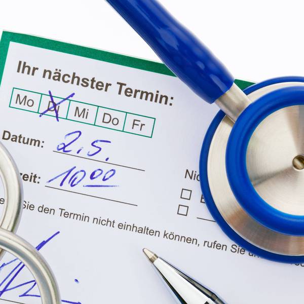 Auf einem Terminvordruck ist ein Termin für einen Arzttermin handschriftlich angekreuzt und notiert; auf dem Zettel liegt ein Stethoskop.