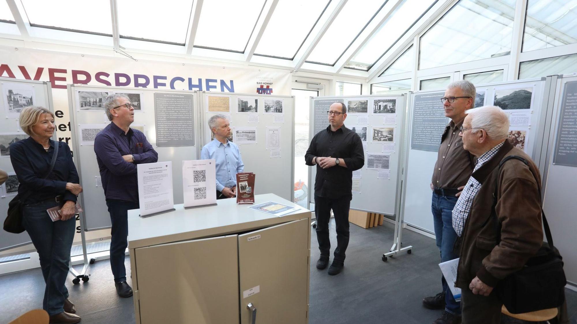 Eine Gruppe von Menschen stehen vor Schautafeln und einem Stahlschrank.