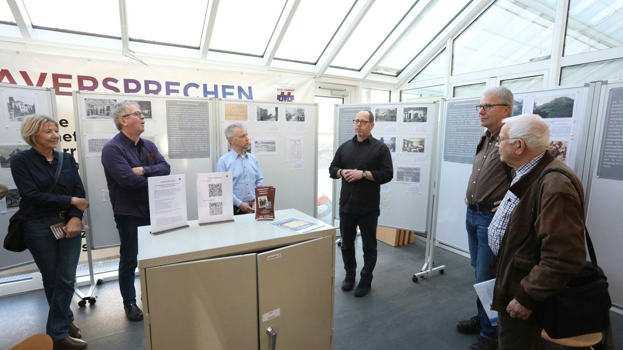 Eine Gruppe von Menschen stehen vor Schautafeln und einem Stahlschrank.