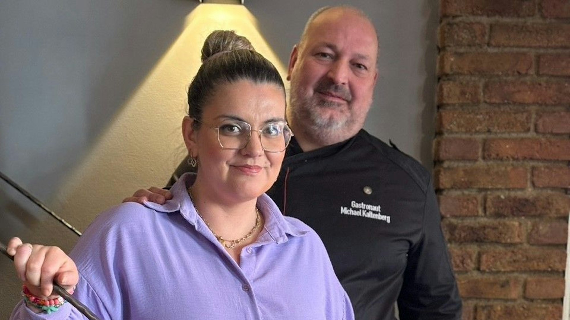 Zwei Menschen stehen vor einer Backsteinwand.