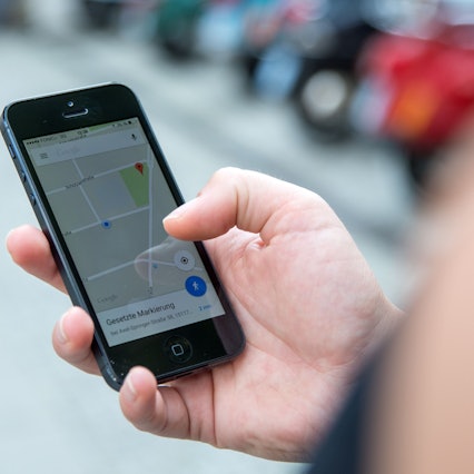 Eine Person schaut auf einem Parkplatz auf ihr Smartphone, auf dem die App Google Maps geöffnet ist