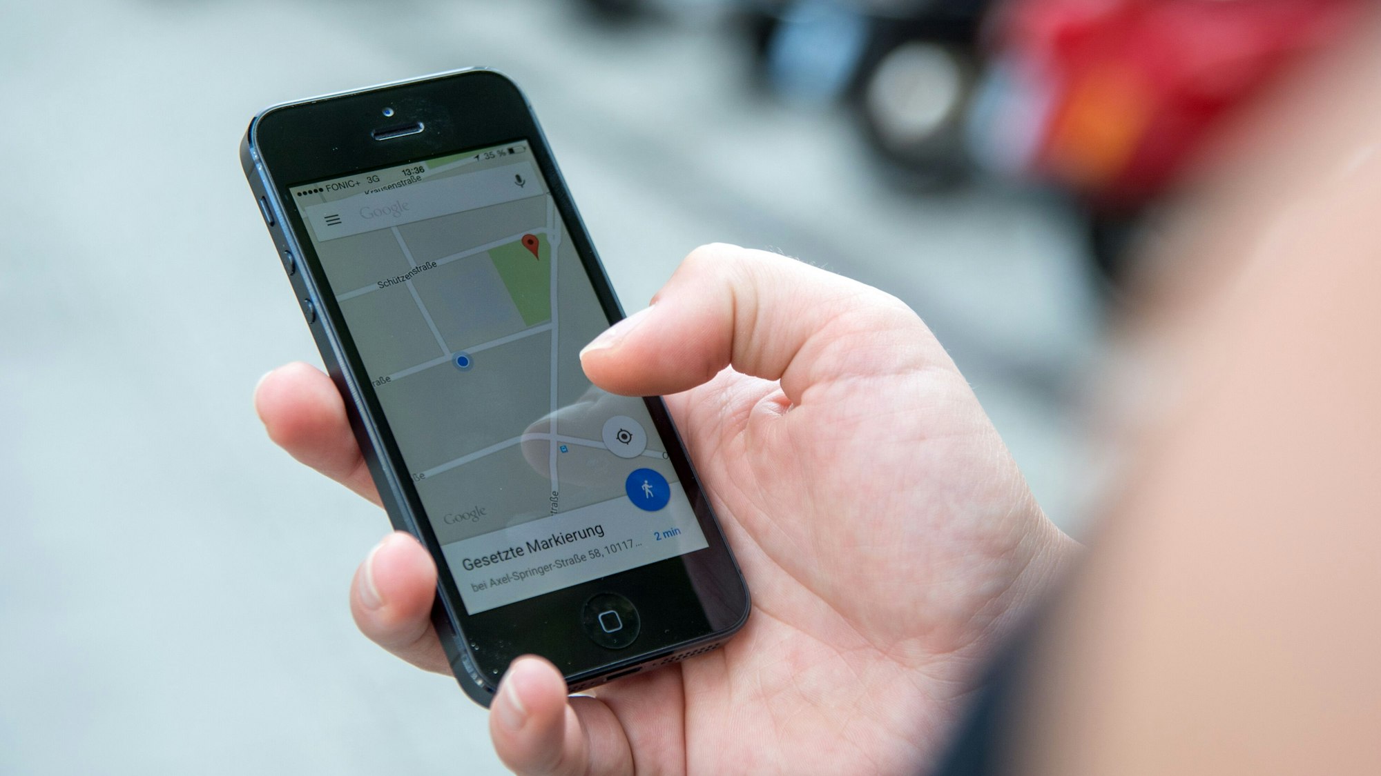 Eine Person schaut auf einem Parkplatz auf ihr Smartphone, auf dem die App Google Maps geöffnet ist